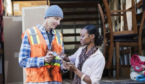 A woman is signing paperwork as a professional mover from a full-service moving company holds the clipboard for her