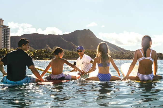 A family of four takes surfing lessons together in the waters off Waikiki, a popular beach in Honolulu, Hawaii.