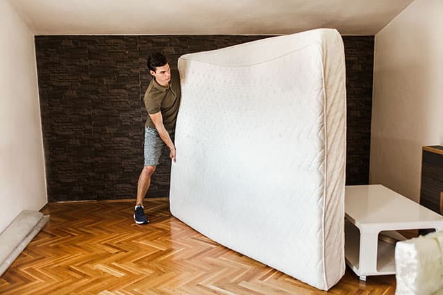 A man is figuring out how to move a mattress into his new bedroom. He is holding the mattress on its side to make it easier to move.
