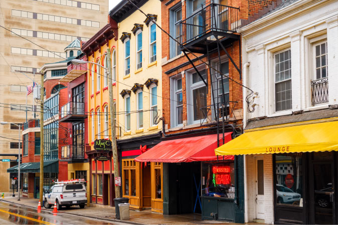 A view of colorful storefronts in Downtown — one of the best neighborhoods in Lexington, KY — featuring red and yellow awnings, fire escapes, and wrought iron balconies.