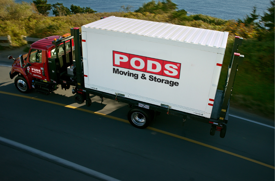 A view of a PODS truck carrying a portable moving container down a highway while it drives to one of the top 2022 moving trends destination.