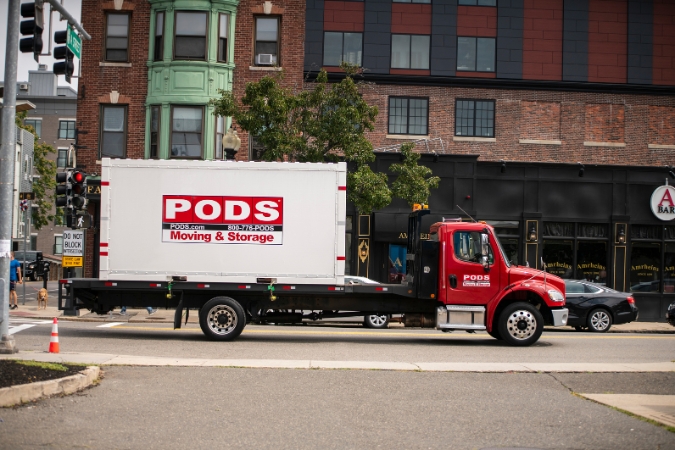 A PODS truck is transporting a portable moving container through city streets as part of a City Service long-distance move.