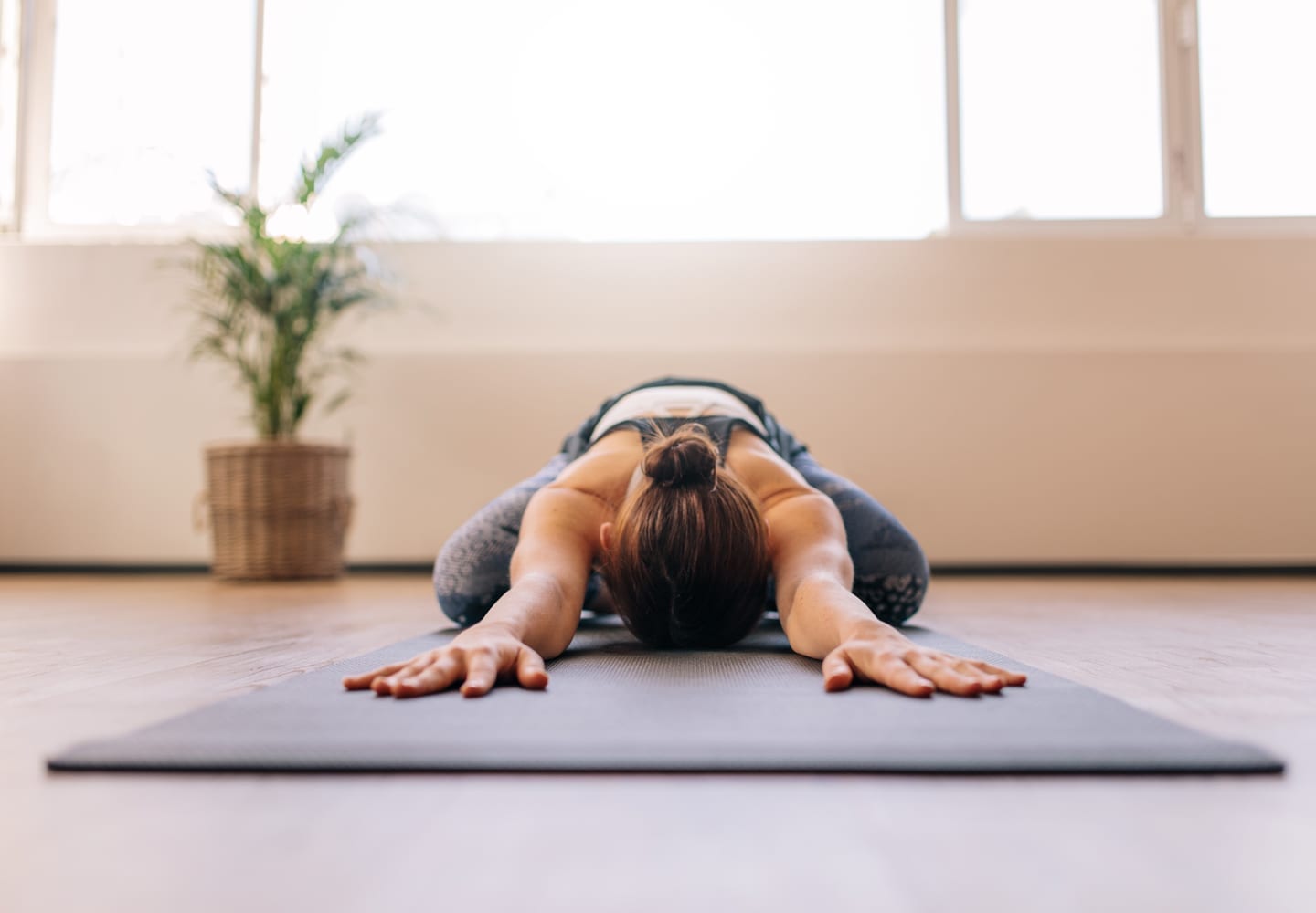 A woman lays on her yoga mat with her arms stretched out as she practices the child's pose.