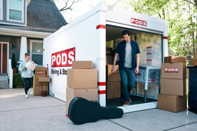 A husband and wife are unloading a PODS portable moving container in the driveway of their new home in one of the best Jersey City neighborhoods.