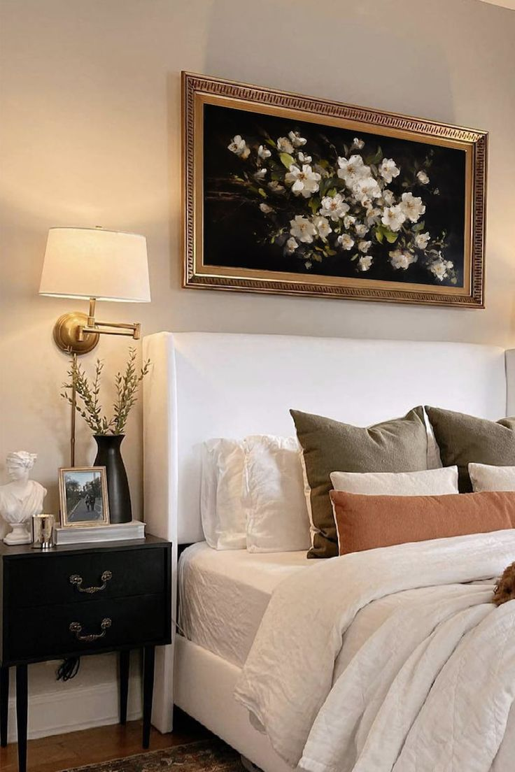 A white bedframe with a framed flower painting over it. 