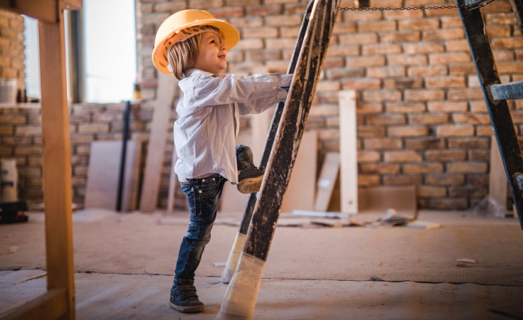 A toddler climbing a ladder with a construction hat on