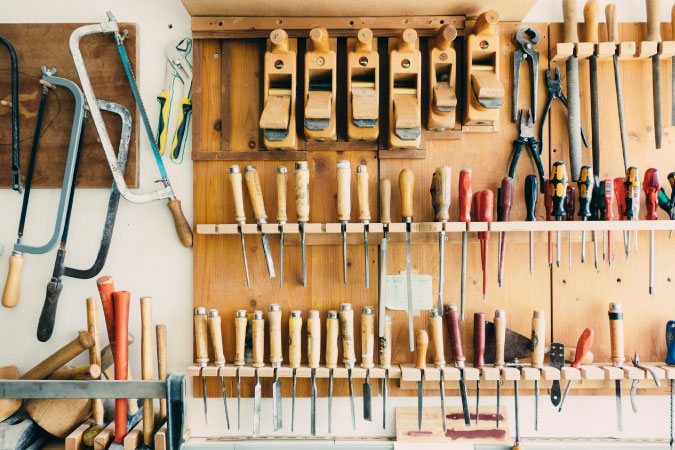 Dozens of handheld tools — like screwdrivers, chisels, and files — are hanging on a wall, a good example of proper shed organization.