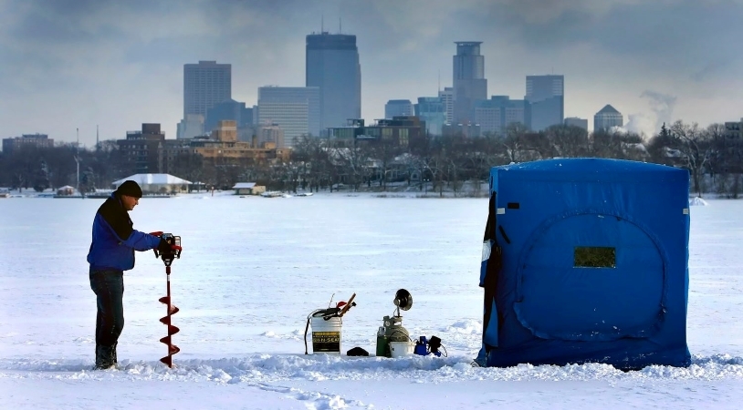 A man is drilling a hole in a frozen Minneapolis lake in preparation for a day of ice fishing.