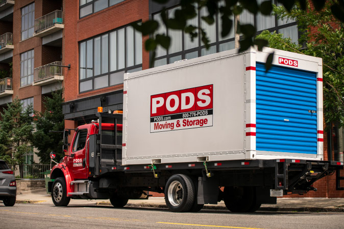 A PODS truck is transporting a portable moving container through city streets as part of a PODS City Service move.