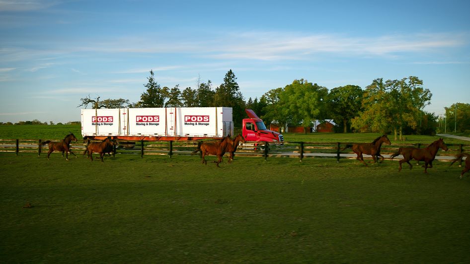 A PODS truck drives past a farm with horses with containers full of items people need with their work relocation packages.