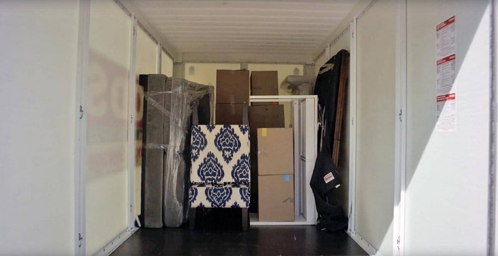 The interior of a PODS Container filled with a table, couch, and various other furniture items.