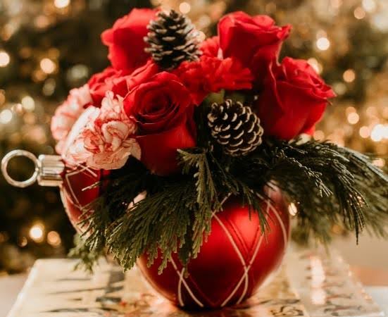 A holiday bouquet with an ornament vase, red roses, pine cones, and greenery — one of the best last-minute Christmas gifts for an out-of-state recipient.