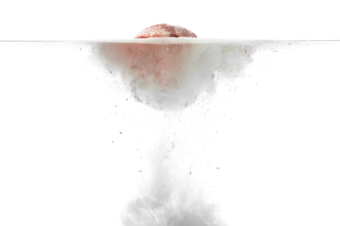 Side view of a DIY homemade bath bomb fizzing up in clear water — one of many fun last minute Christmas gifts you can make at home.