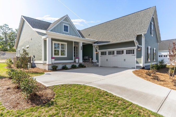 A gray Craftsman-style home, popular in Wilmington, NC, neighborhoods, featuring a long driveway and landscaped lawn shrubbery.