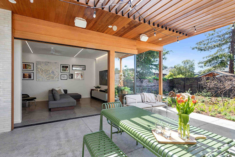  indoor/outdoor entertaining patio with overhead wooden trellis, green picnic table and bench, and orange flowers in a vase