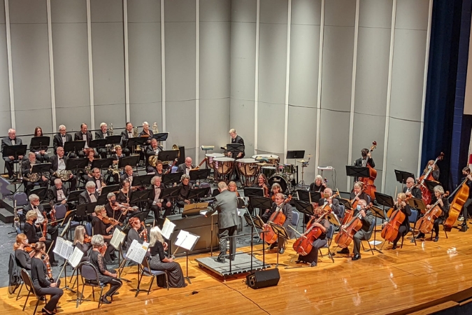 An orchestra performs on stage at the North Port Performing Arts Center as the conductor leads musicians during a symphony performance.