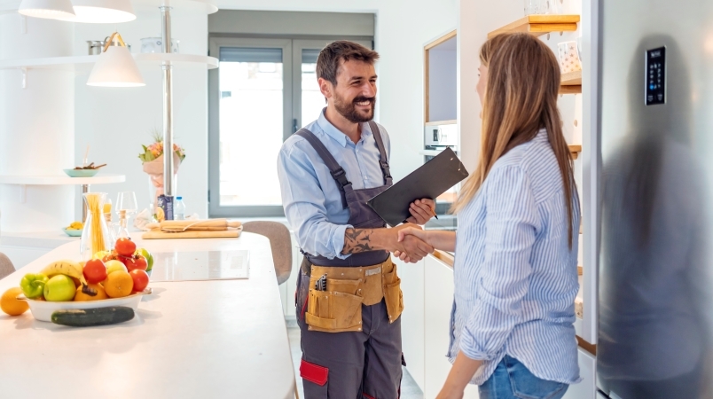 A homeowner and a contractor are standing in a kitchen, shaking hands, The contractor will be renovating the kitchen for the homeowner to make the layout more user-friendly.