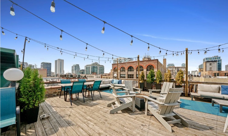 A rooftop patio with a view of the Chicago skyline features matching deck chairs, tables, and plants.