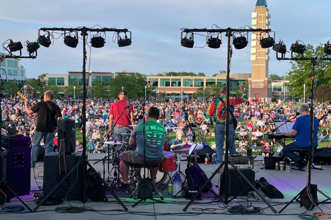 View from the back of the stage of a live music show in Aksarben Village — one of the best Omaha neighborhoods — with hundreds of people watching from an expansive green lawn.