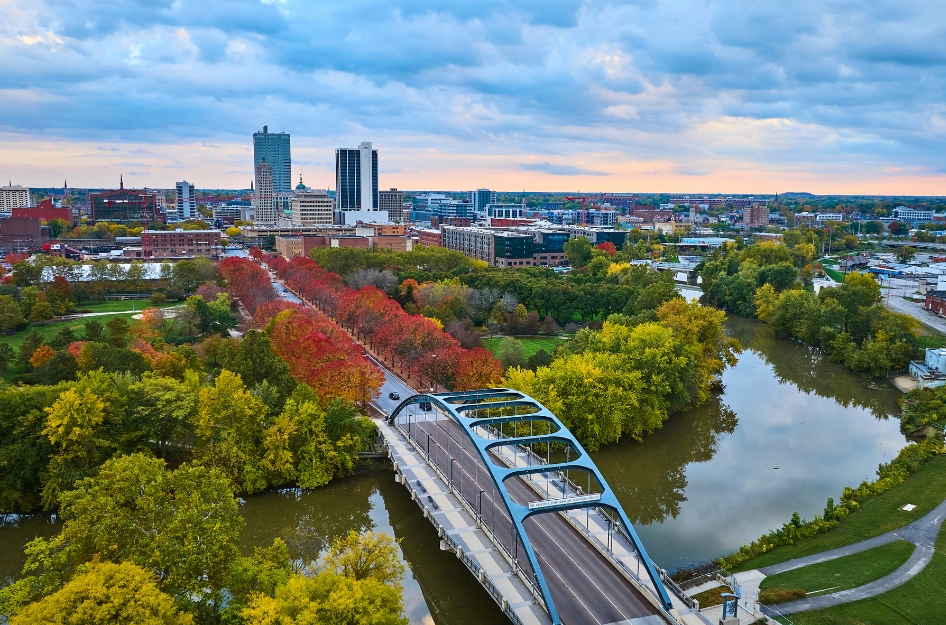 Sunset view of downtown Fort Wayne featuring the city skyline, vibrant autumn leaves, and the Martin Luther King Bridge over St. Marys River — a lovely sight for those living in Indiana.