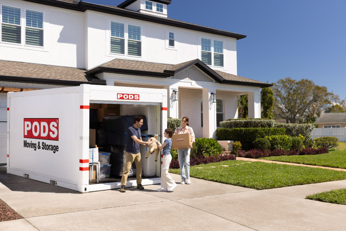 A family of three is using PODS to move cross-country, loading up their portable moving container in the driveway.