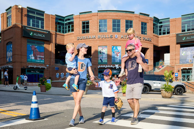 A family of five is crossing a street in Durham, NC, on a sunny day out in the city.
