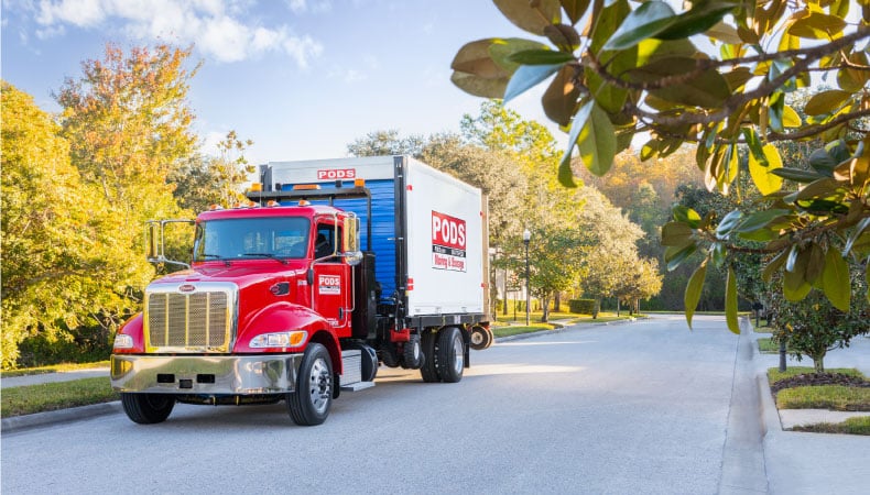 A PODS Moving & Storage truck transporting a PODS portable moving container through a residential street in Edmonton.