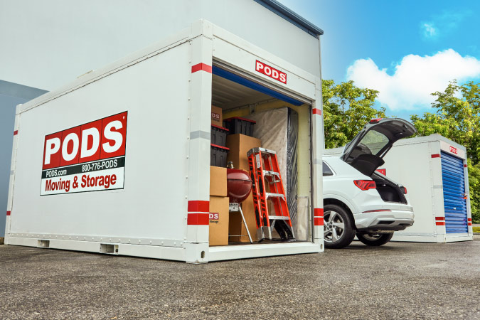 A PODS portable storage container is loaded up with household items beside a white car with an open trunk, illustrating where to store stuff during a remote work stint.