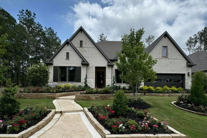 A light brick home in Conroe, Texas, featuring steep gables with narrow windows and black shutters and garage door for accent.