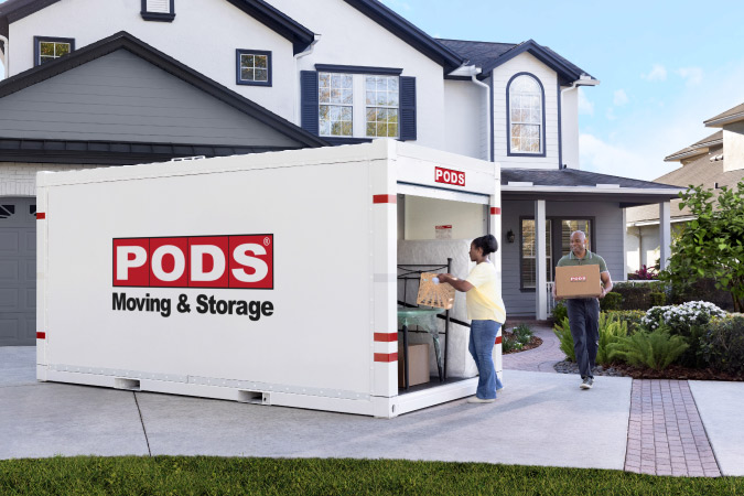 A couple is loading boxes into their PODS portable moving container, which is positioned conveniently in their driveway.