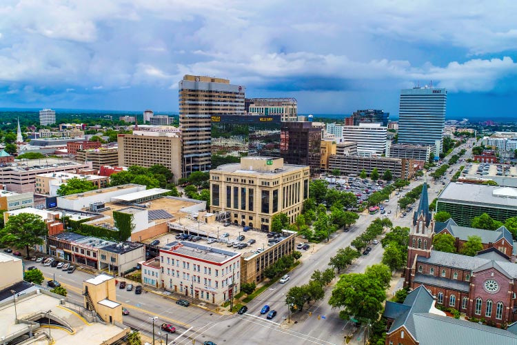 Aerial view of downtown Columbia, South Carolina. There’s a mix of tall and squat city buildings, as well as clusters of mature trees growing along streets and between city blocks.