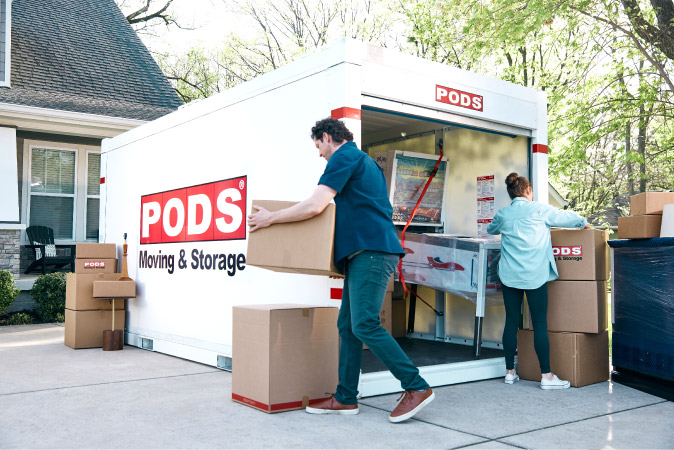 A couple is unloading moving boxes from a PODS portable moving container in the driveway of their new home after moving to Lincoln, Nebraska.