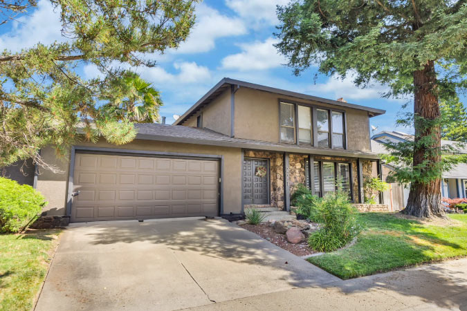 Exterior view of a split-level duplex in Pocket-Greenhaven — one of the best neighborhoods in Sacramento — featuring a two-car garage, covered porch, and mature redwood tree in the front yard.