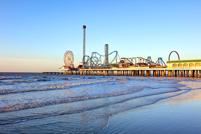 Galveston Island’s historic pleasure pier in the late afternoon. Carnival rides stand tall on the pier as the sun bathes the pier in a warm glow.