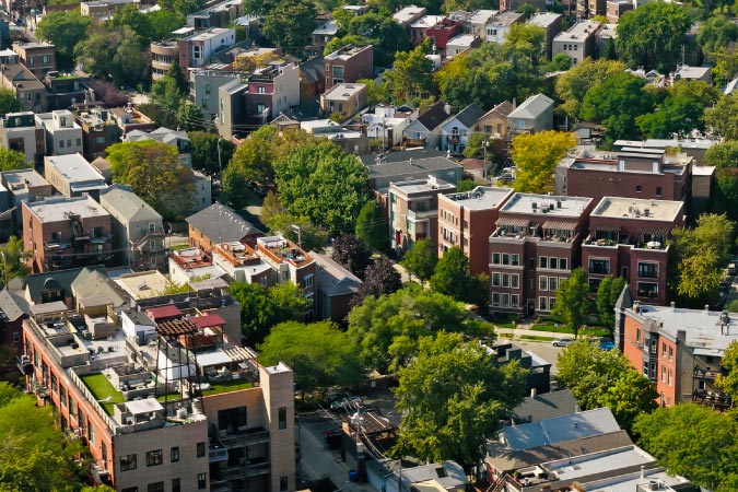 Aerial view of West Town — one of the safest neighborhoods in Chicago — featuring an abundance of greenery growing between multi-family buildings, many made with red brick.