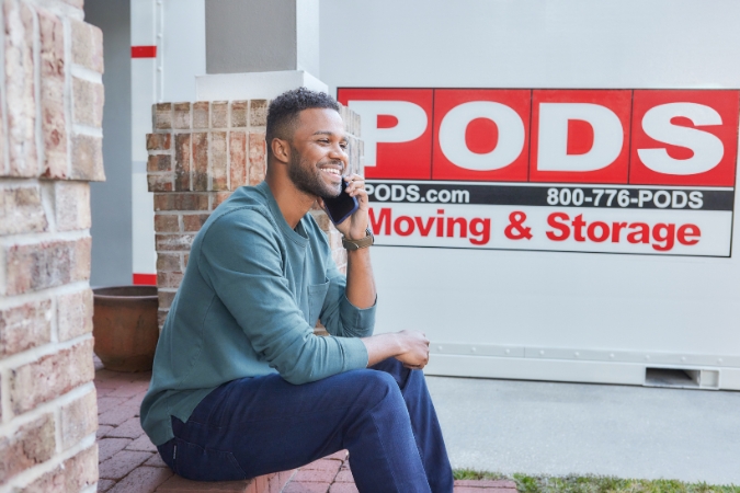 A young man is sitting on the front porch of his Baton Rouge home speaking with a PODS agent on his cell phone after moving to one of the best Baton Rouge neighborhoods.