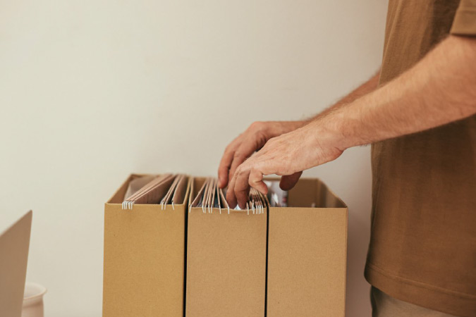 Close-up of a man in a brown shirt rifling through filing boxes at home.