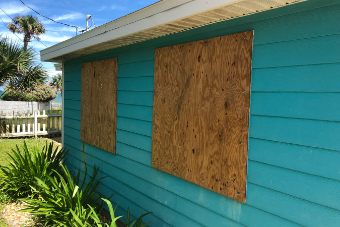 Exterior of a blue, one-story residential home with windows that have been boarded up for disaster preparedness.