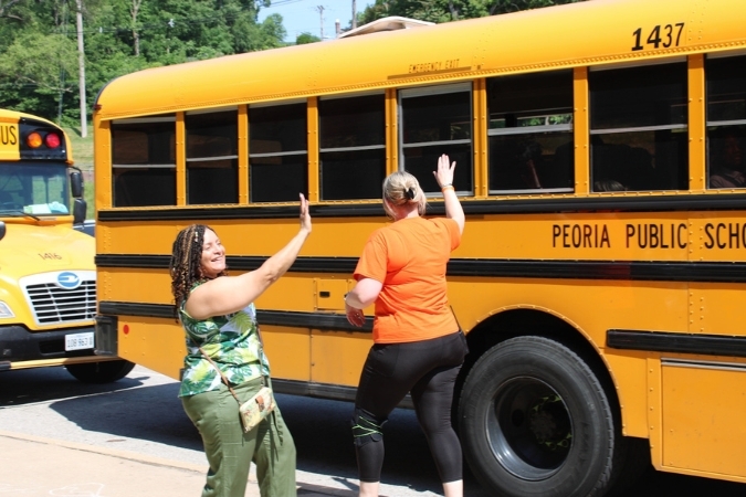 Two teachers in Illinois — one of the best states to teach in — wave at students on school buses as they leave the school.
