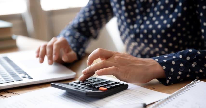 Close-up of a woman’s hands as she uses a calculator to add up her estimated relocation expenses so she can negotiate a job relocation package.