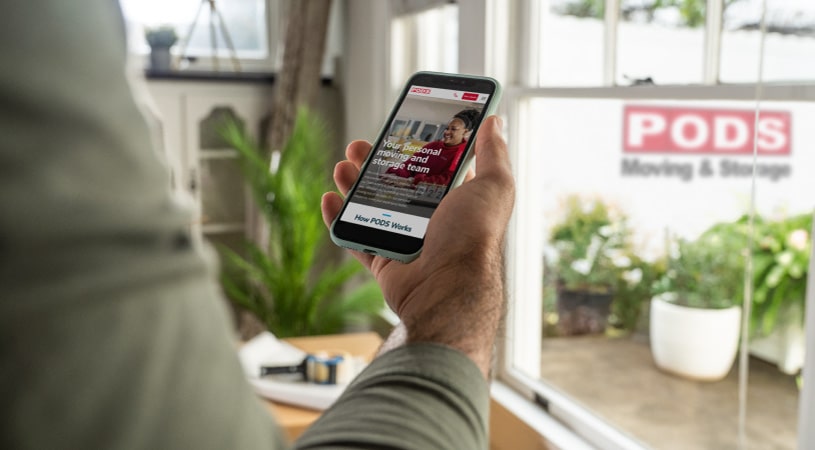 A man using his phone to access the PODS website to get a quote on a moving and storage container.