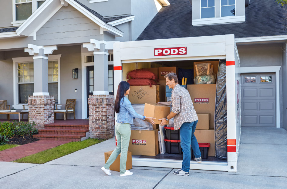 A man and woman are loading the final box into the PODS portable moving container in their driveway after choosing PODS vs. Full-Service Movers.