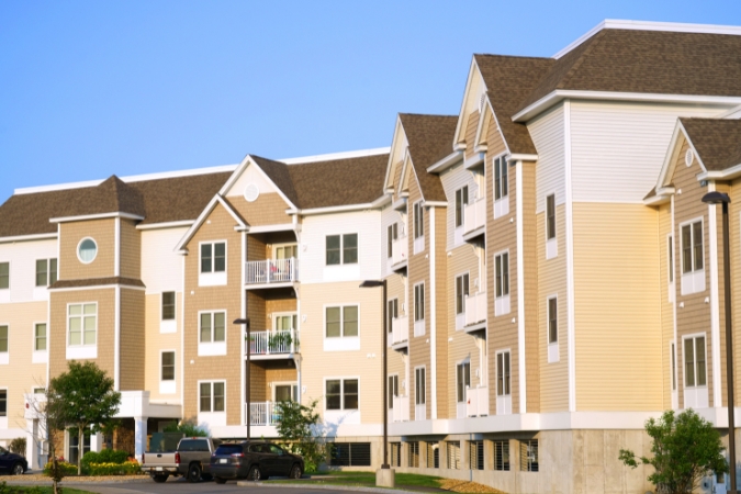 A modern apartment complex with beige siding, private balconies, and a parking area, highlighting affordable rental options for those moving to Greensboro, NC.