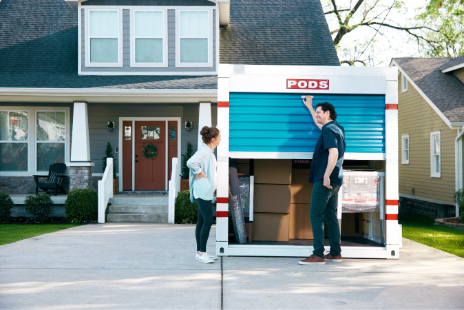 A couple is standing together at the front of a PODS container in their driveway, preparing to unload it into their new home in one of the best neighborhoods in Wilmington, NC.