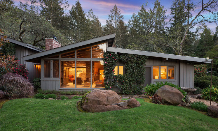 A one-story, mid-century home in Montecito Heights. Lush ivy is growing up the front of the home, the yard is landscaped with short grass and decorative boulders, and there are tall trees in the back.