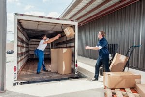 Two men carelessly tossing a box to each other inside a truck