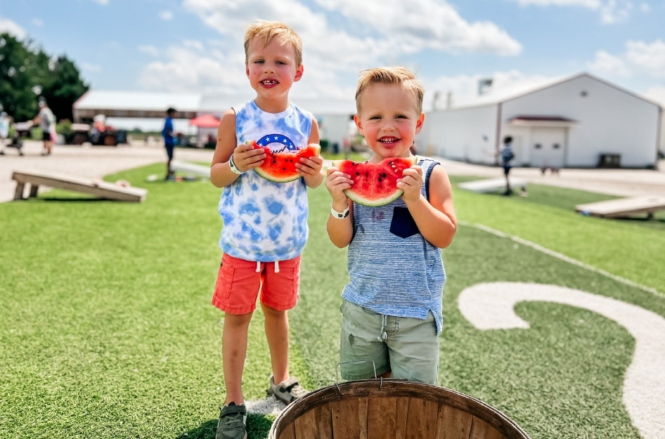 Two little boys enjoy watermelon slices at Nelson Produce Farm in Omaha, Nebraska.