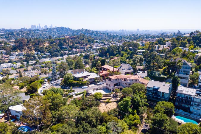 Aerial view of the Los Feliz neighborhood in Los Angeles on a sunny day, featuring the Downtown L.A. skyline in the distance
