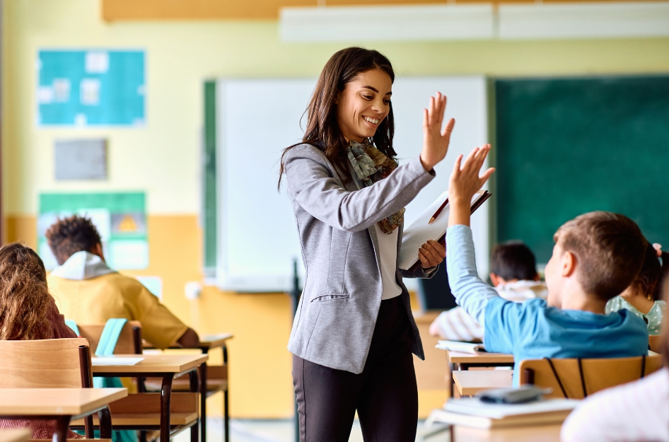 A smiling teacher high-fives a student in a classroom with a low student-teacher ratio, highlighting why location matters when considering the best states for teachers.