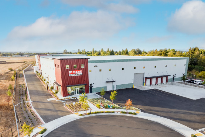 Aerial view of a secure PODS Storage Center in California, featuring a fenced perimeter, multiple garage doors, and a large “PODS” sign.